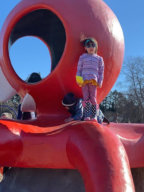 Young girl in sunglasses standing on a large concrete octopus play structure. Victoria BC with kids.