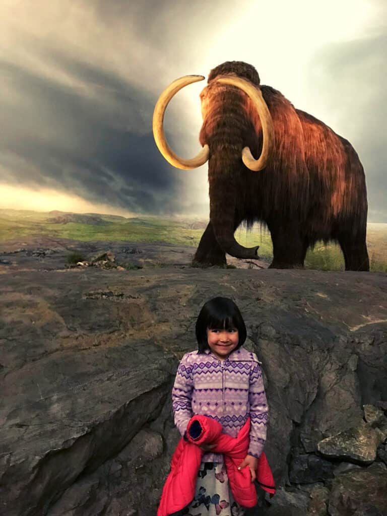 Royal BC Museum, Victoria Wooly Mammoth exhibit with young girl smiling in front. 
