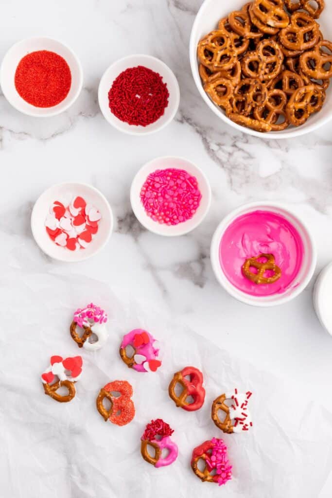 Decorating pretzels by dipping in red, white and pink candy melts with Valentine's sprinkles for decoration.