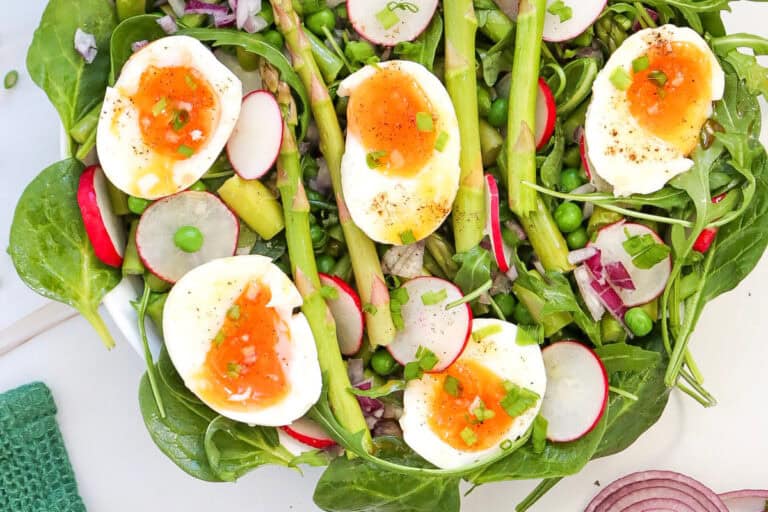 Overhead view of asparagus pea salad with spinach, radish slices, herbs and halved boiled eggs.
