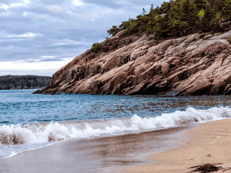 Roacky shore and sandy beach with waves in Acadia National Park. 