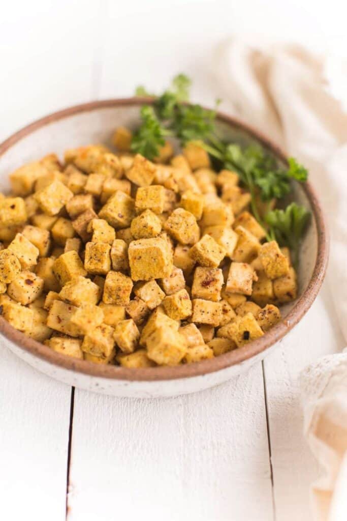 A ceramic bowl of small air fried tofu cubes, with parsley as garnish.