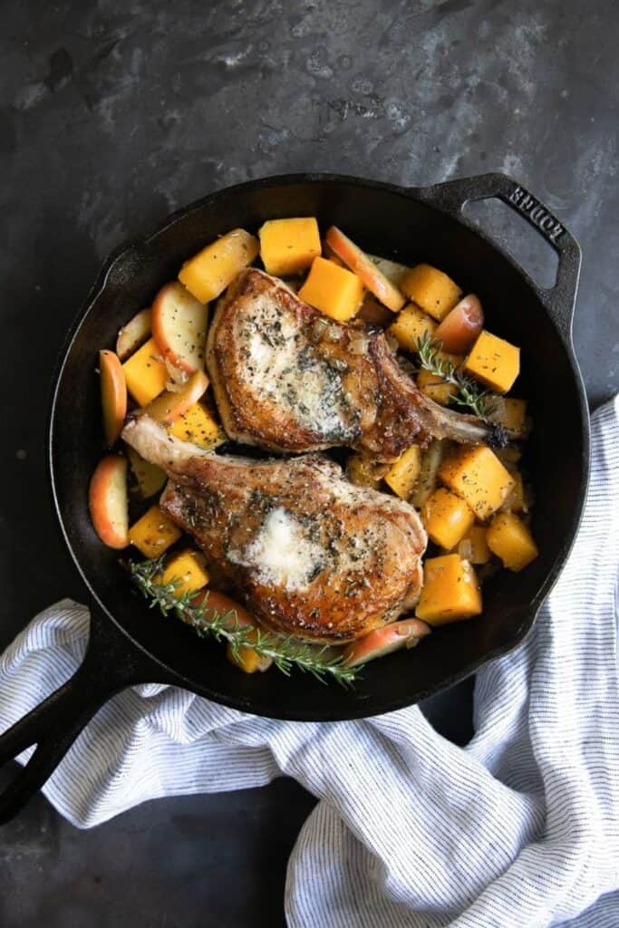 Cast iron pann with two apple cinnamon pork chops and butternut squash cubes.