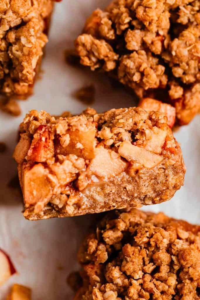 Close-up of a chewy apple crumble bar packed with tender apple chunks, cinnamon spice, and a golden oat topping. The warm, rustic texture makes it an inviting treat perfect for fall baking apple recipes.