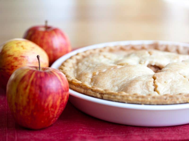 Autumn bucket lits idea bake and Apple pie in white dish beside 3 apples.