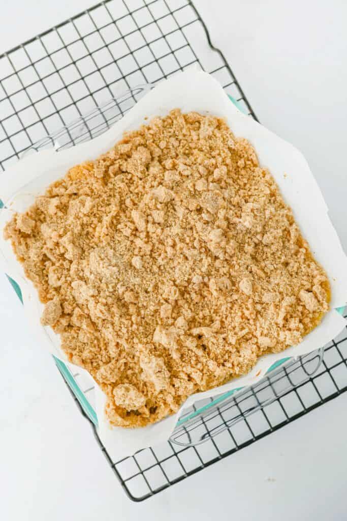 Unbaked apple crumble bars covered with a thick cinnamon crumble topping in a parchment lined square baking dish. The assembled bars are ready to go into the oven.