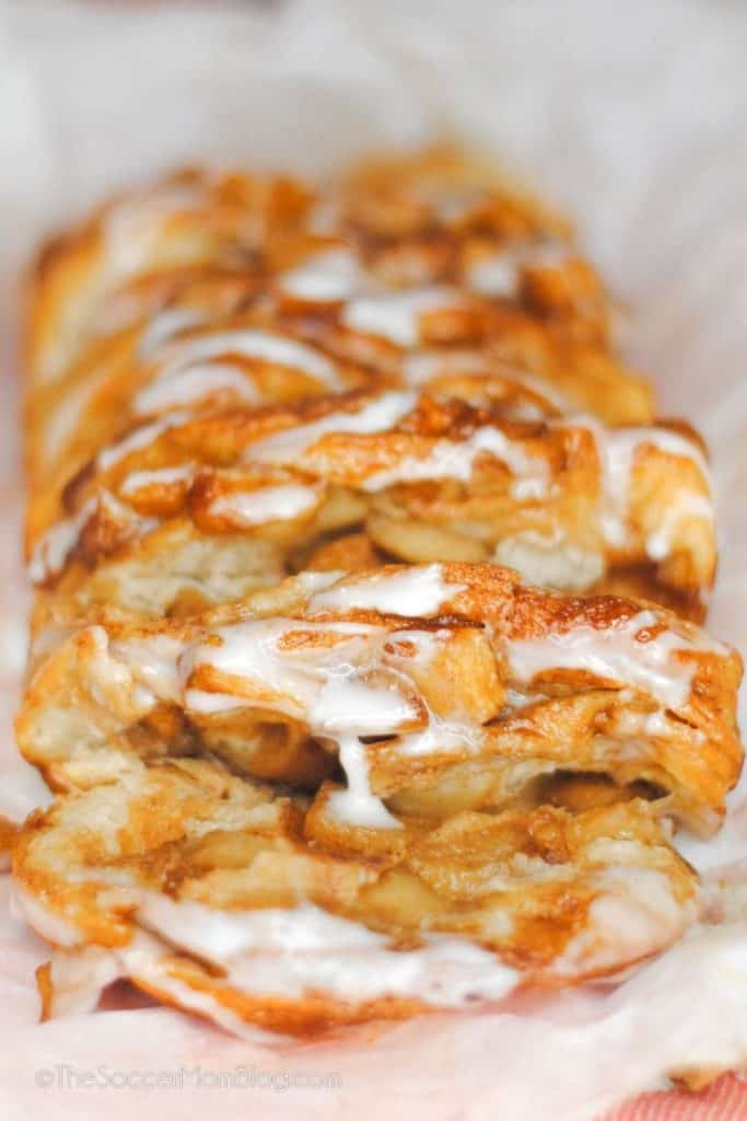 Close-up of a warm apple pull-apart bread drizzled with vanilla glaze, with layers of cinnamon-coated apples nestled between golden, flaky dough. This cozy treat is perfect for showcasing fall apple desserts with its gooey texture and sweet spiced aroma.