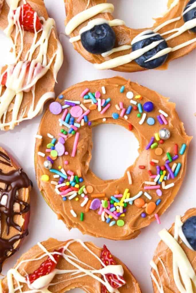 Apple slices cut into ring shapes are topped with creamy peanut butter and decorated with colorful sprinkles, blueberries, strawberries, and drizzles of white and dark chocolate. These fun, festive snacks offer a healthy Thanksgiving dessert alternative that’s both kid-friendly and visually appealing.