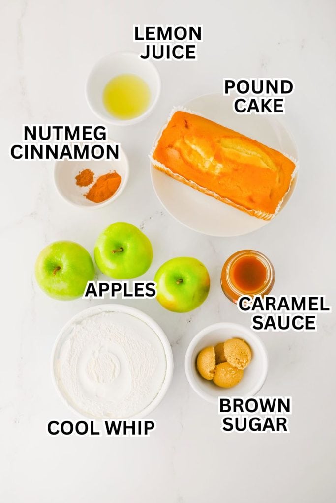 Flat lay of apple trifle ingredients labeled and arranged on a white surface, including green apples, pound cake, Cool Whip, brown sugar, caramel sauce, lemon juice, cinnamon, and nutmeg. Each item is placed in a bowl or dish