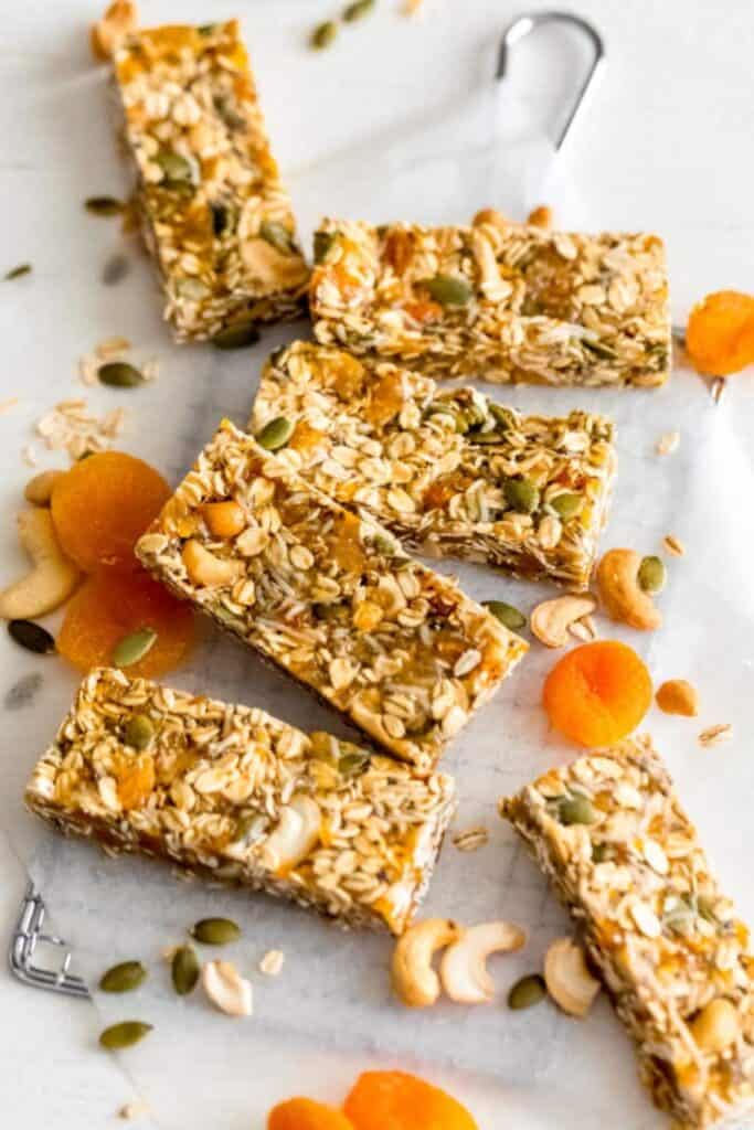 Homemade apricot cashew bars cut into rectangles and arranged on a light marble surface, packed with rolled oats, chopped dried apricots, cashews, and pumpkin seeds.