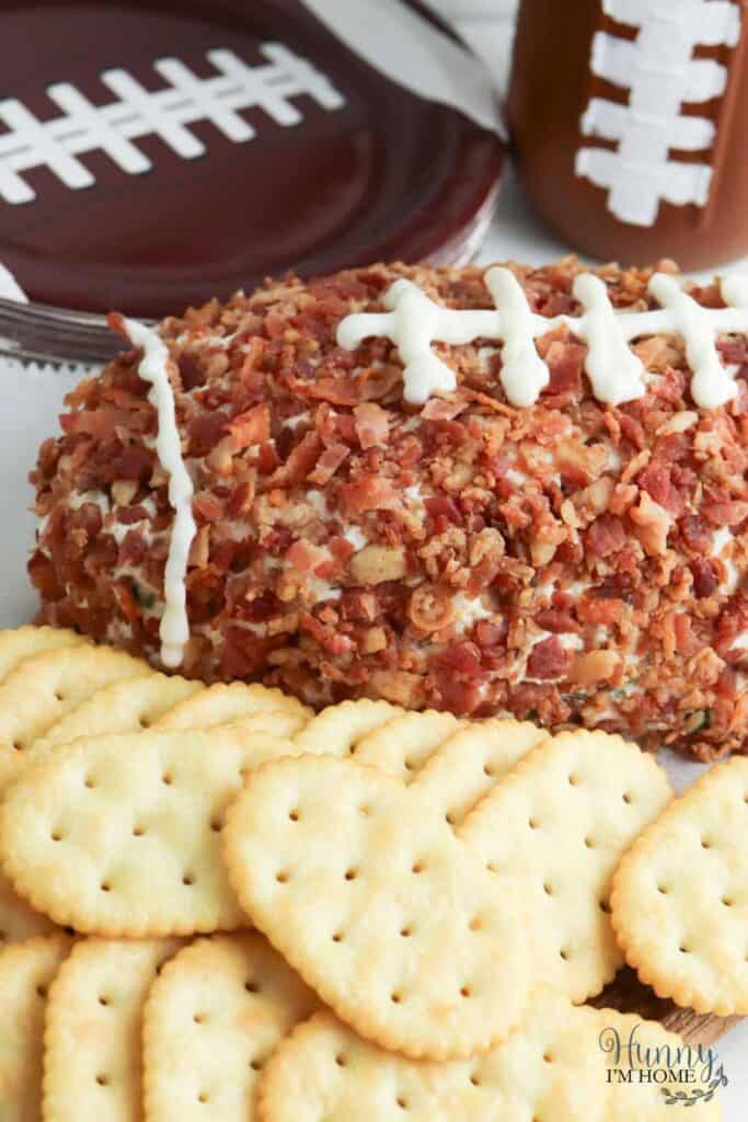 Close up of a bacon cheeseball shaped as a football with round crackers in front of it. 