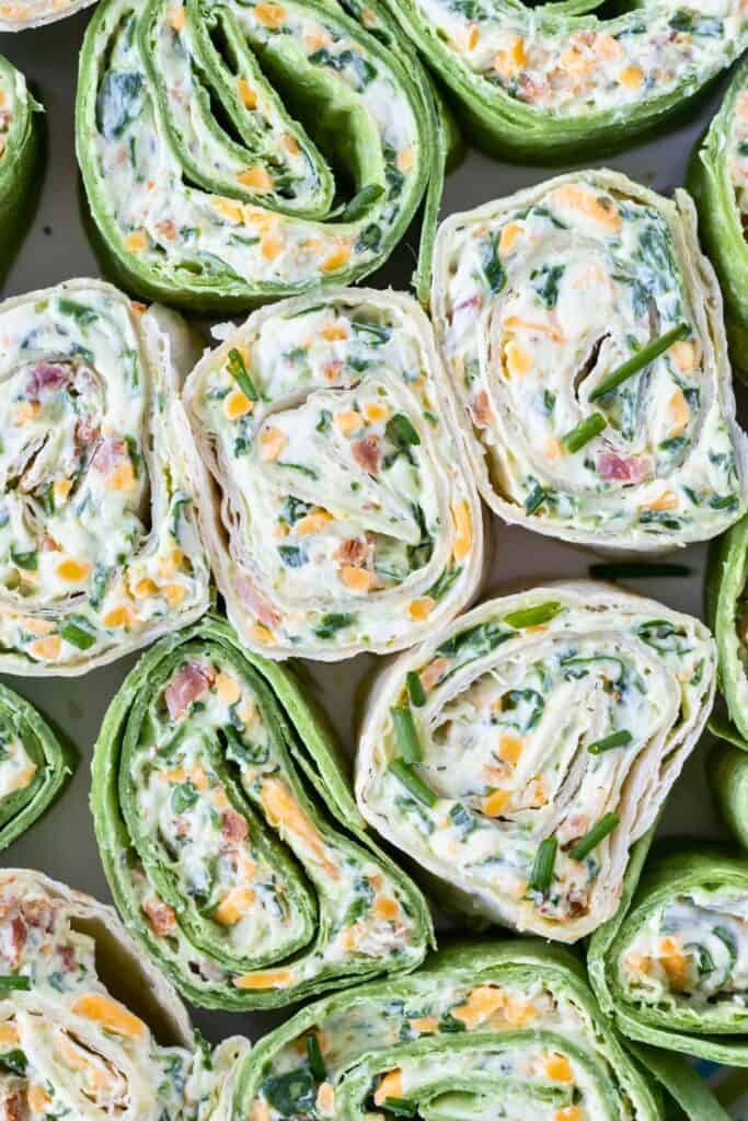 Bacon spinach rollups sliced into pinwheels and arranged on a platter, showing layers of soft tortillas filled with a creamy cheese mixture, chopped spinach, bacon, and shredded cheese. The close up view highlights the colorful spiral pattern and bite sized shape that makes these rollups an easy make ahead snack.
