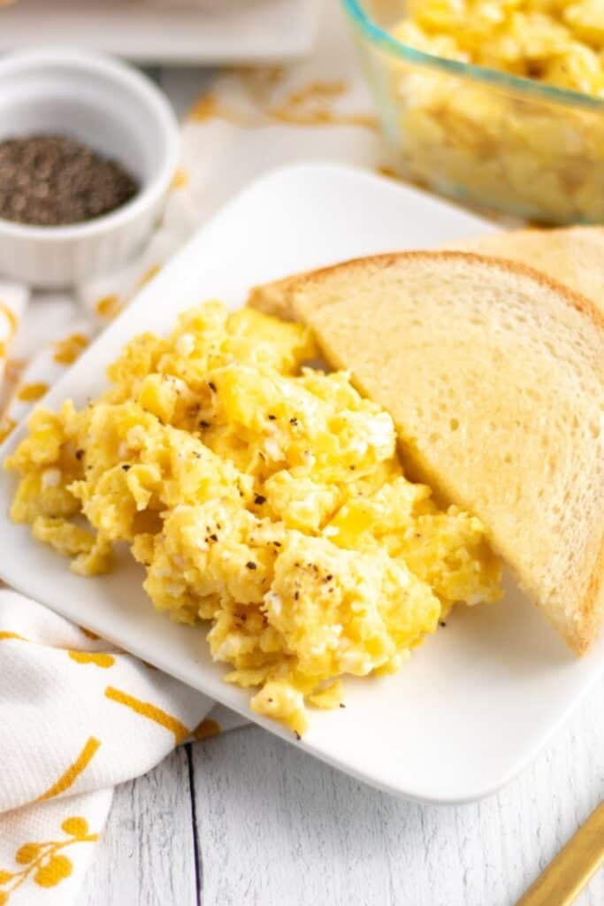 plare of baked scrambled eggs and white bread toast. 