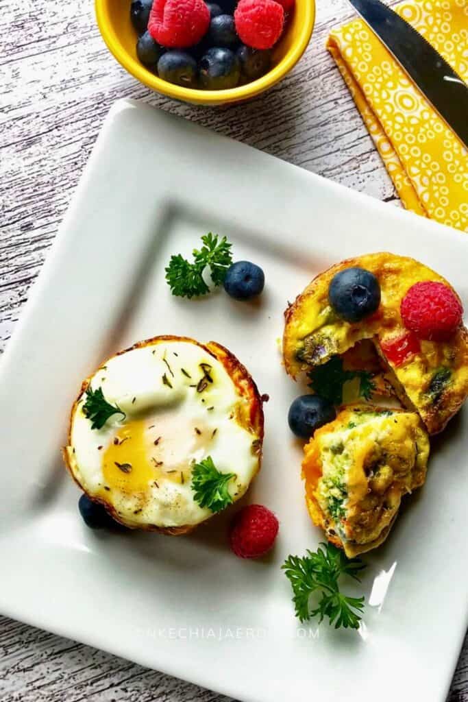 Baked sweet potato egg cups served on a white plate with one whole cup and one cut open to show a soft egg center and vegetable filling. Fresh berries and parsley garnish the plate highlighting these baked sweet potato egg cups as a colorful balanced protein breakfast option.