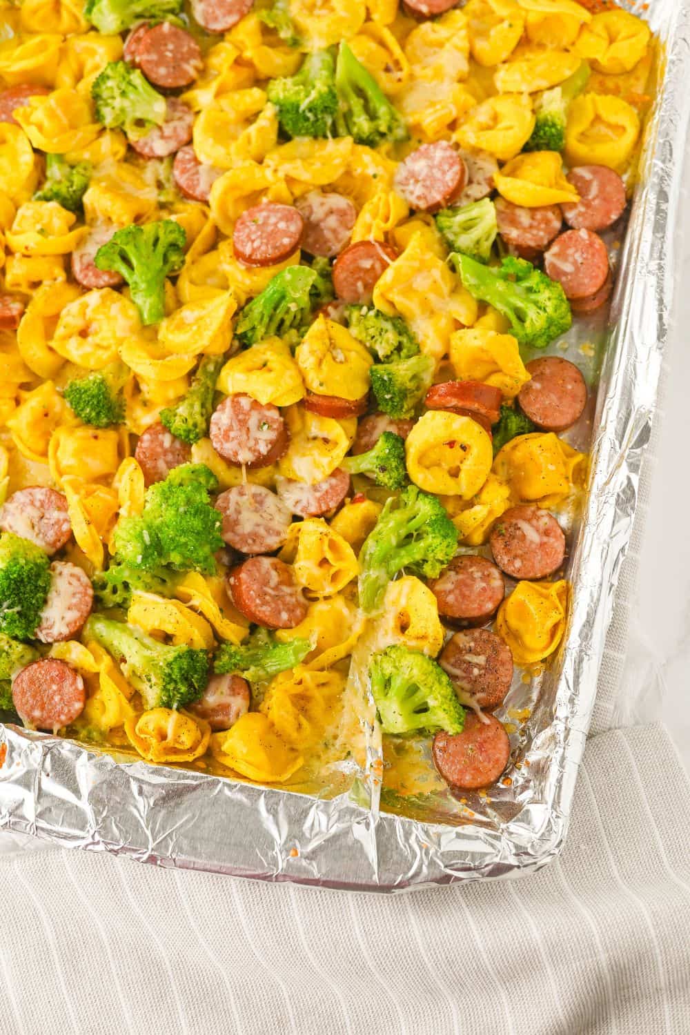 Overhead view of a sheet pan with bakked tortellini, broccoli and sausage pieces. 