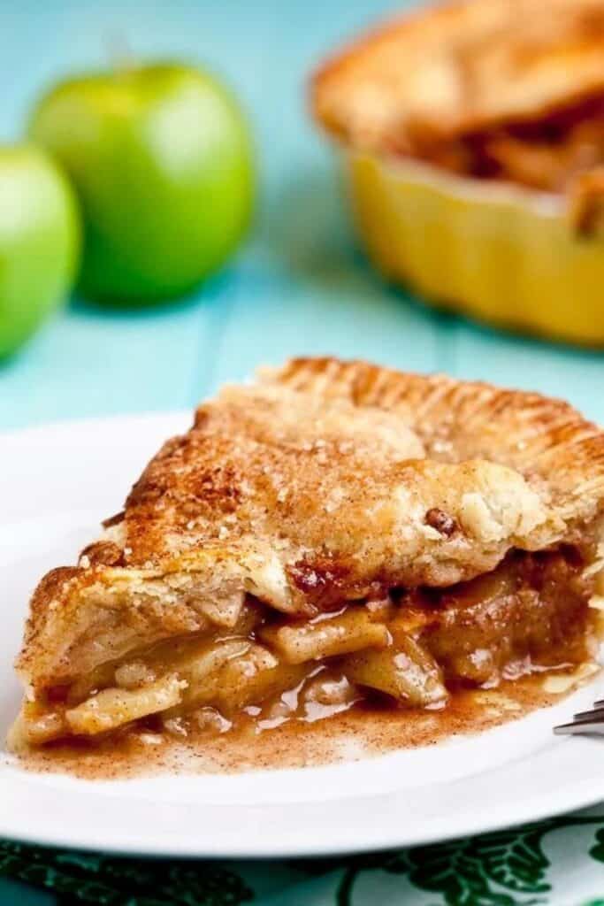 Slice of apple pie with flaky crust on a plate. 