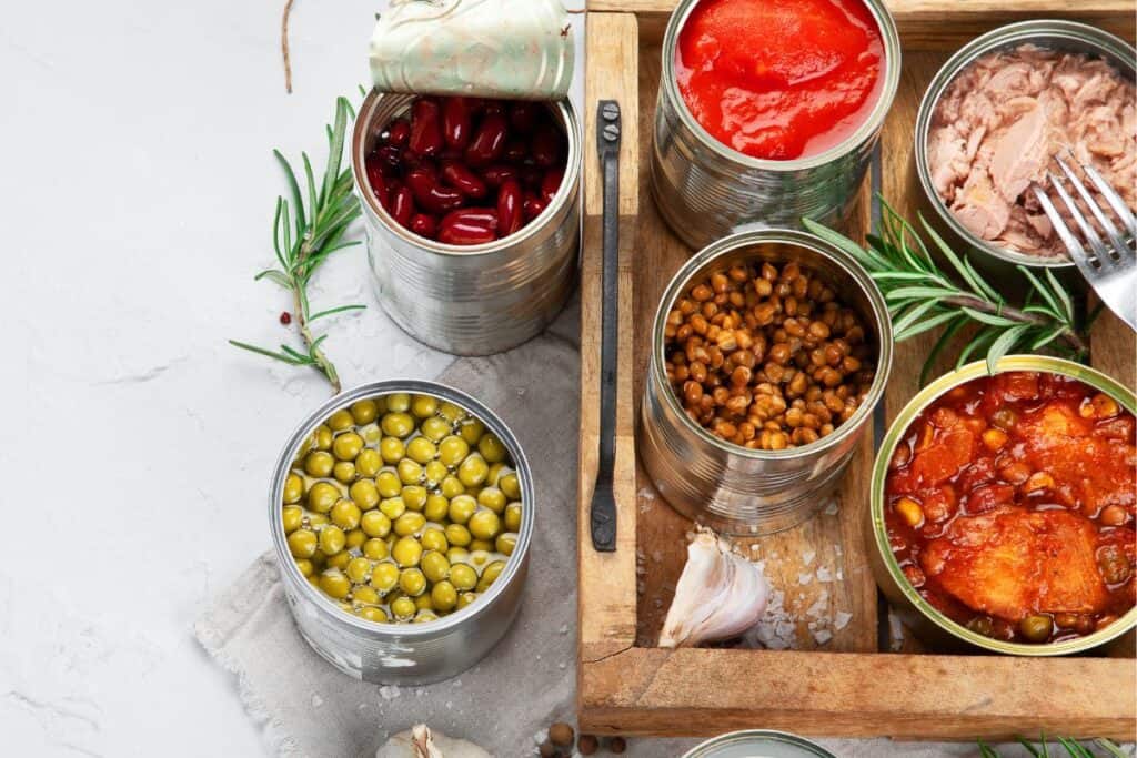 Canned camping foods of beans, meat, tomatoes in wooden tray.