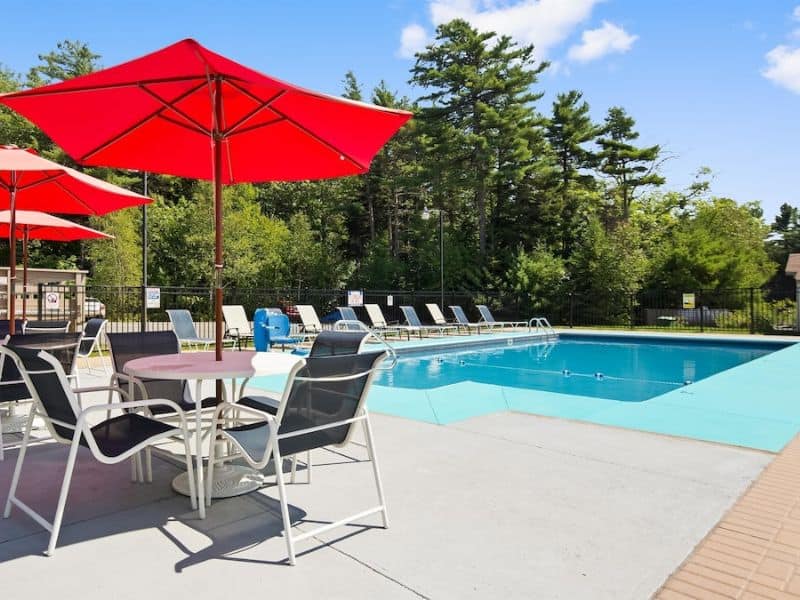 Colorful patio tables, chairs & umbrellas by outdoor pool on sunny day.