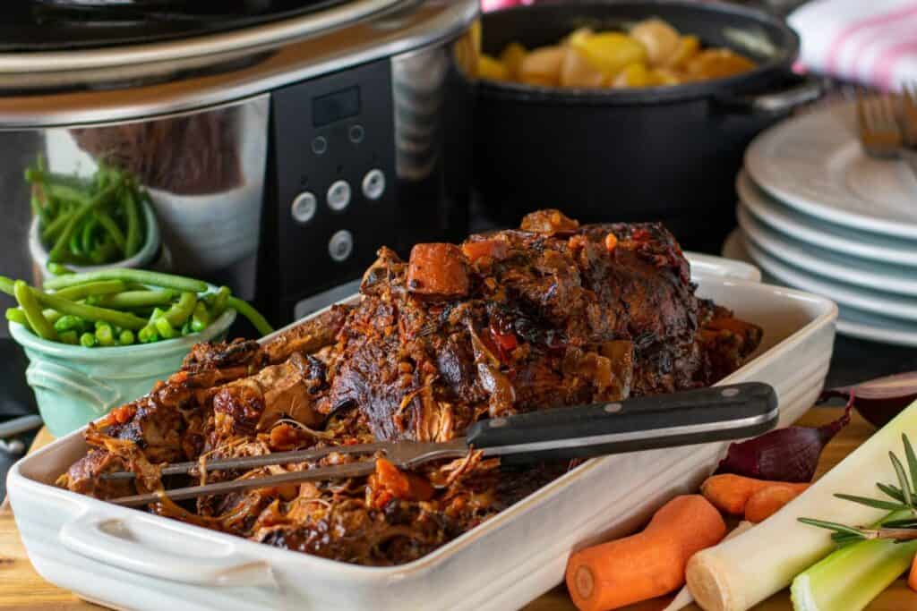 Slow cooked roast surround by carrots, potatoes and sloww cooker machine.