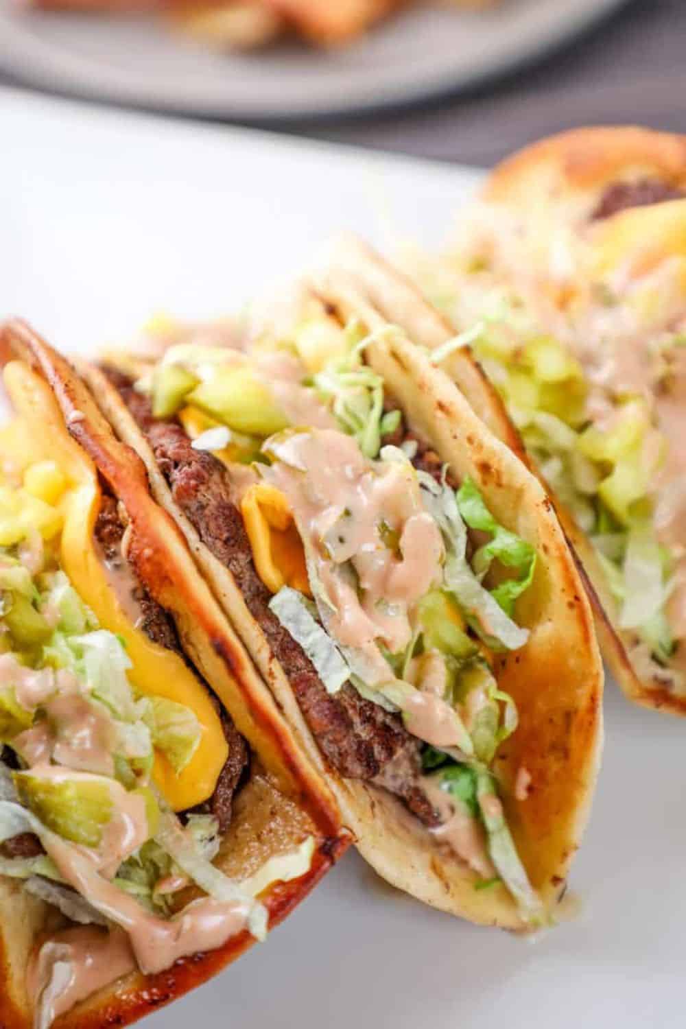 Crispy Big Mac smashburger tacos filled with seasoned beef, melted American cheese, shredded lettuce, diced pickles, and creamy burger sauce. The folded tortillas are toasted until golden and served taco style, highlighting the cheesy filling and classic burger-inspired toppings.