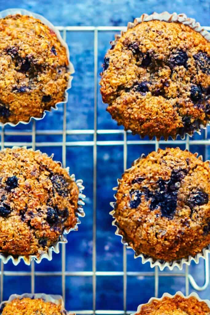 Close up of blueberry bran muffins cooling on a wire rack with a hearty textured top and deep golden brown color. 