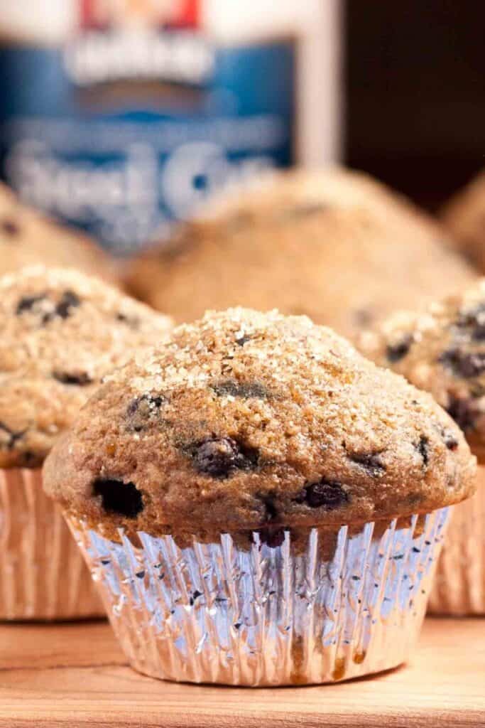 Close up of blueberry oatmeal muffins with golden brown domed tops and a light sprinkle of sugar. The hearty texture from oats is visible in the crumb while juicy blueberries dot the moist interior.