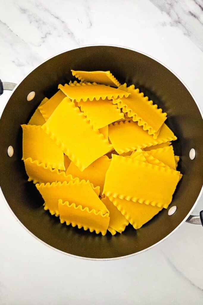 Overhead view of broken lasagna noodles placed in a large pot to cook until tender.
