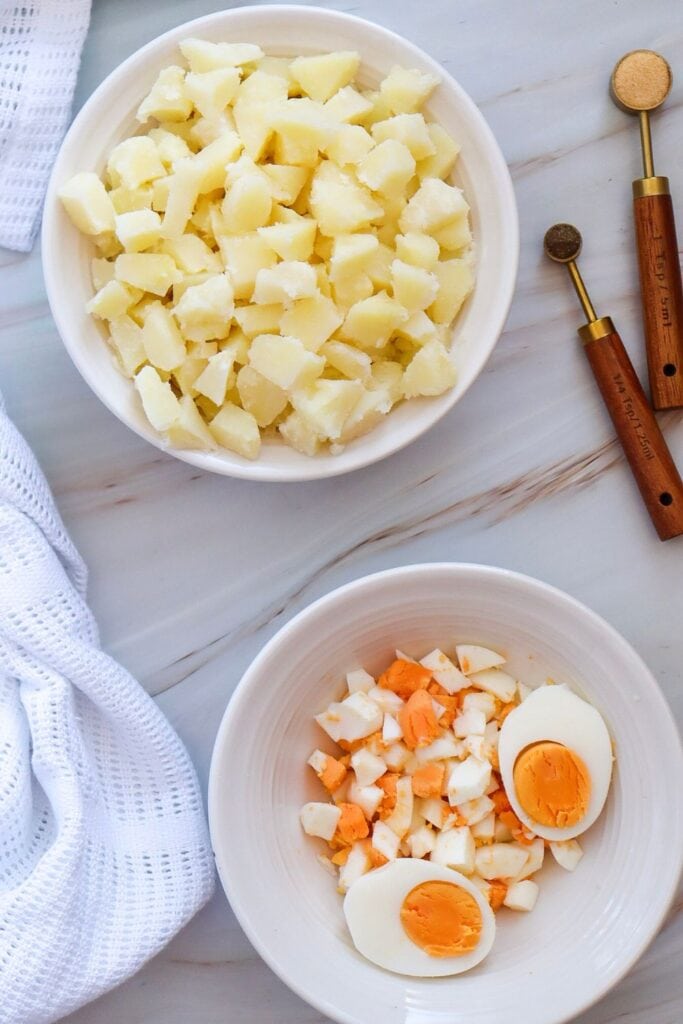 Process shot of two bowls containing diced boiled eggs and cubed potatoes. 