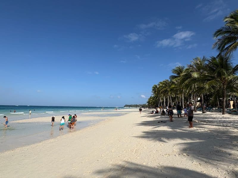 Tropical white sand beach with families playing in the ocean in Boracay Philippines
