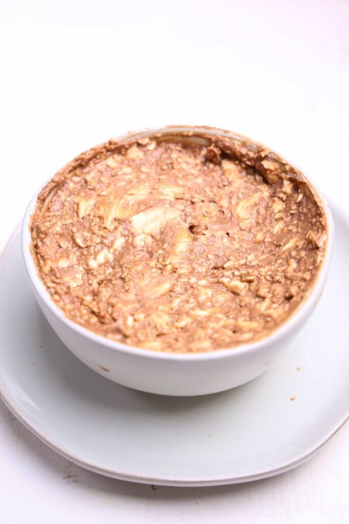 A white bowl filled with a swirled mixture of nutella and cream cheese dip, showing a marbled texture with visible chunks. The bowl is placed on a simple white plate against a light background.