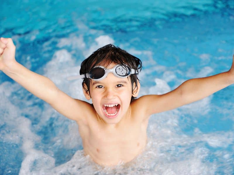 Young boy raising armas and smiling at swimming pool