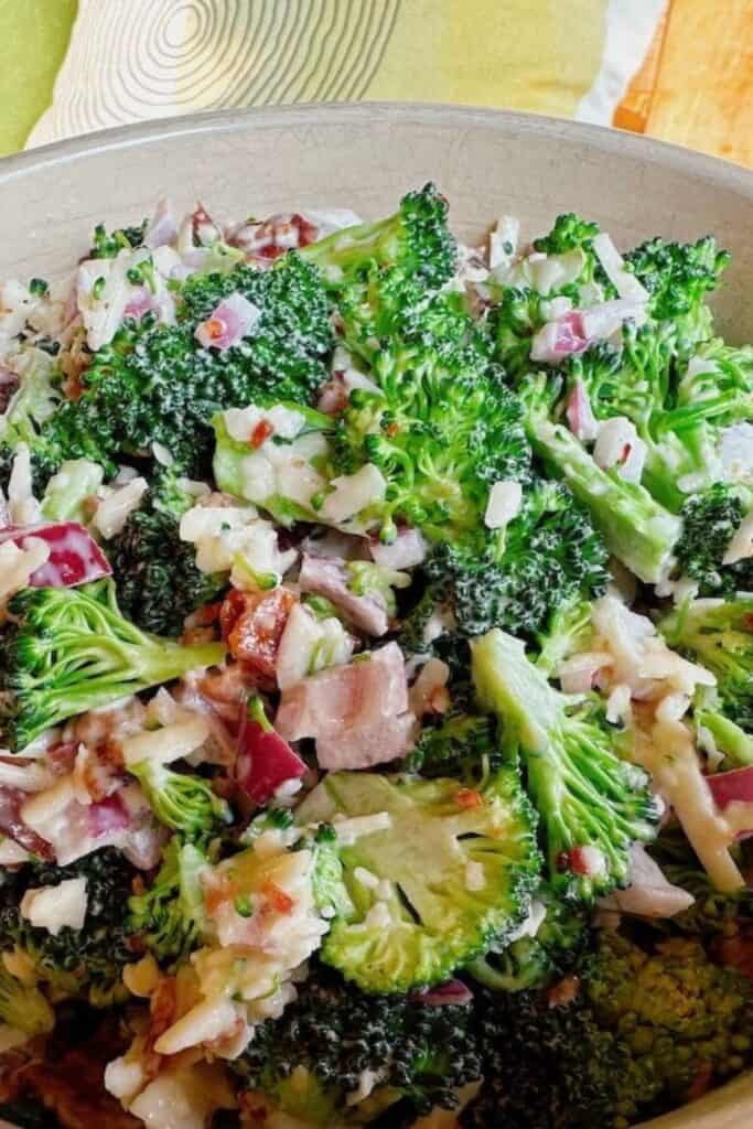 Broccoli salad made with fresh crisp broccoli florets tossed with chopped red onion, bacon pieces, shredded cheese, and sunflower seeds in a creamy dressing.