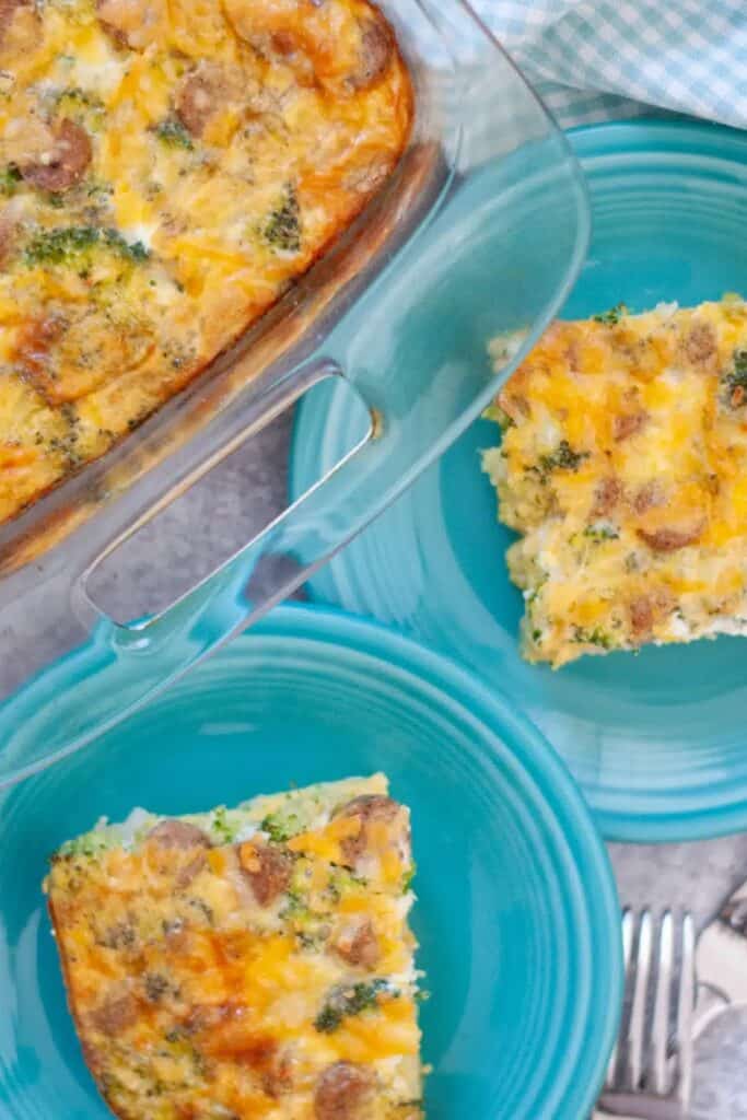 Broccoli sausage egg bake sliced into squares and served on bright blue plates, with the remaining casserole visible in a clear glass baking dish.