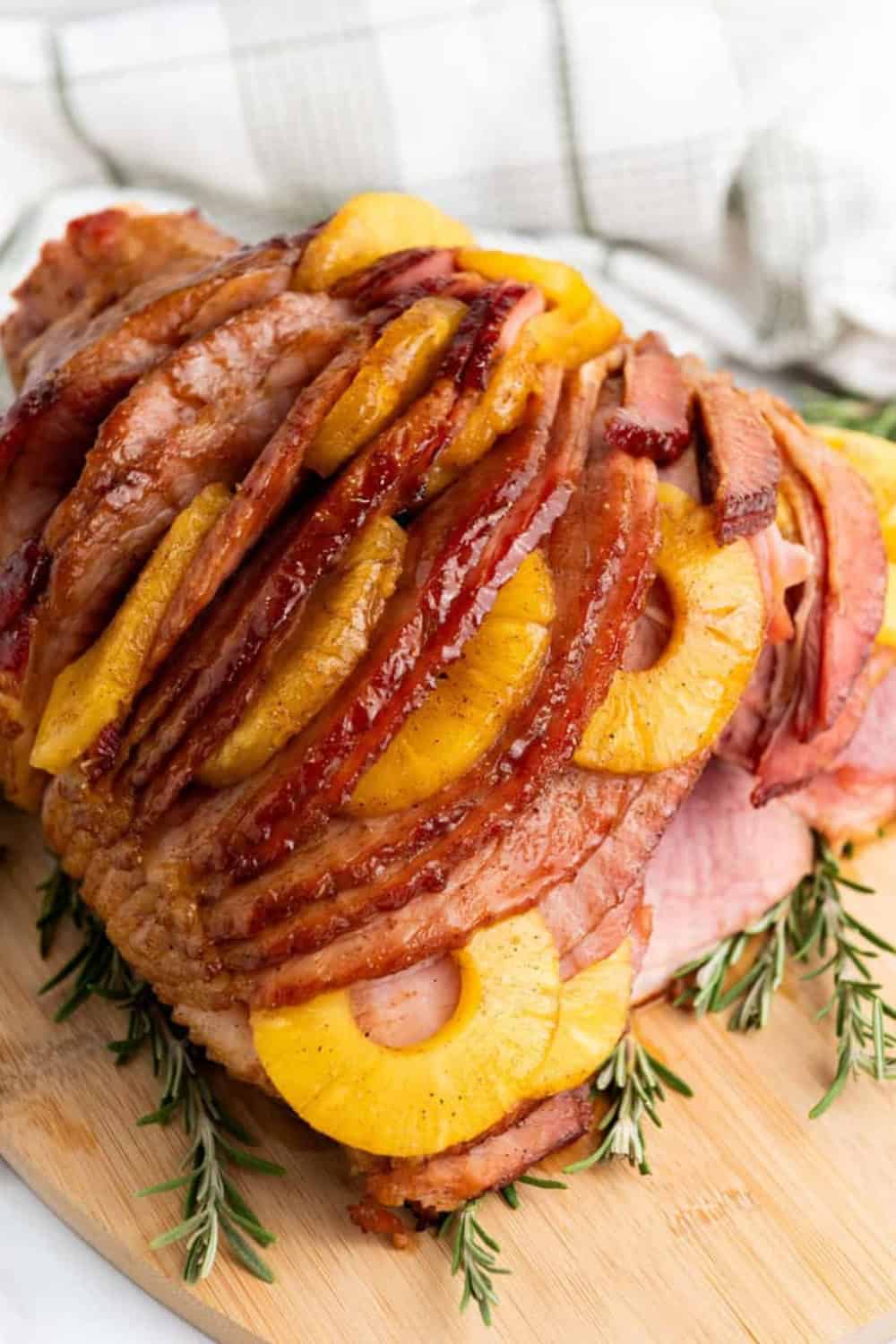 A glazed Brown Sugar Pineapple Ham sliced and layered with golden pineapple rings, coated in a glossy brown sugar glaze and served on a wooden board with fresh rosemary for a festive Christmas potluck main dish.