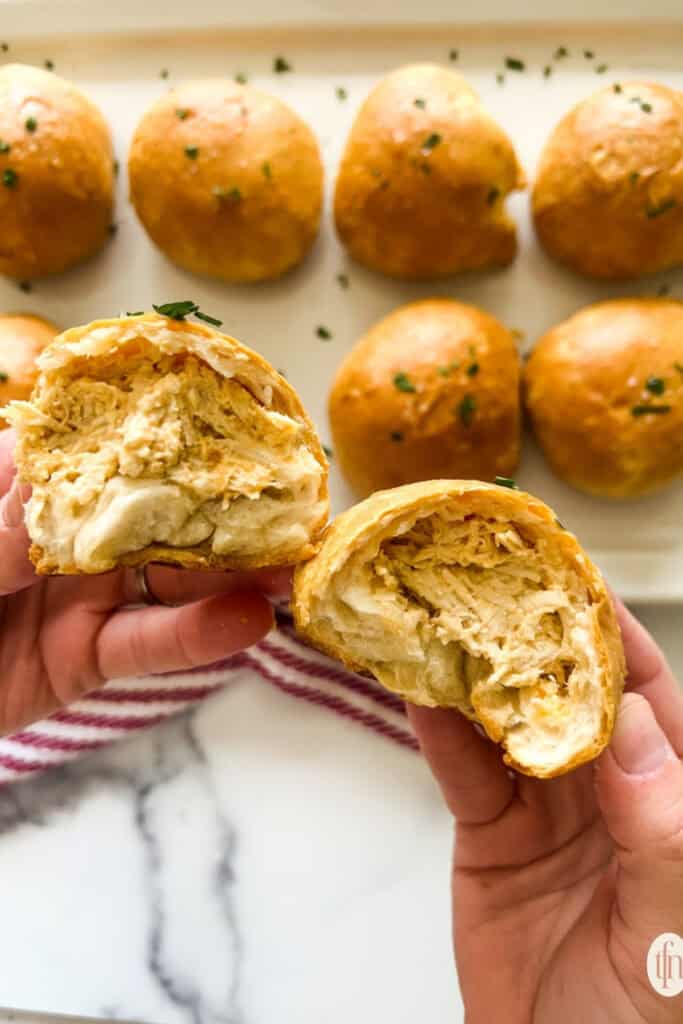 A hand breaking open the Buffalo Chicken Bites which are round buns stuffed with chicken. 