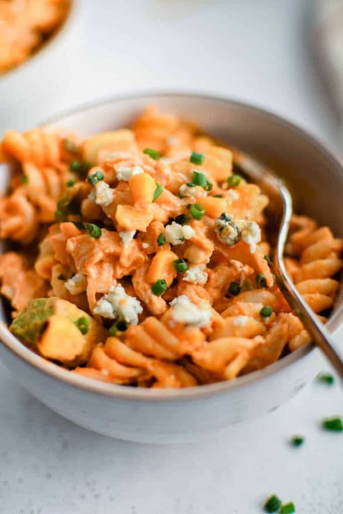 Small bowl of rotini pasta buffalo chicken salad topped with crumbled blue cheese. 