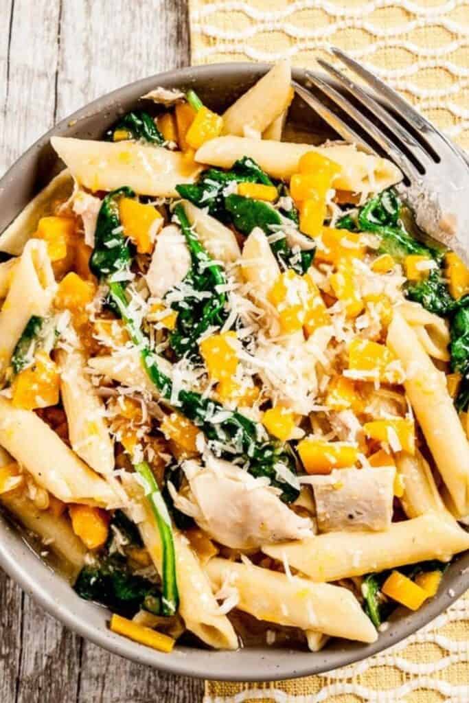 Bowl of penne pasta with butternut squash, spinach, chicken and parmesan cheese. 