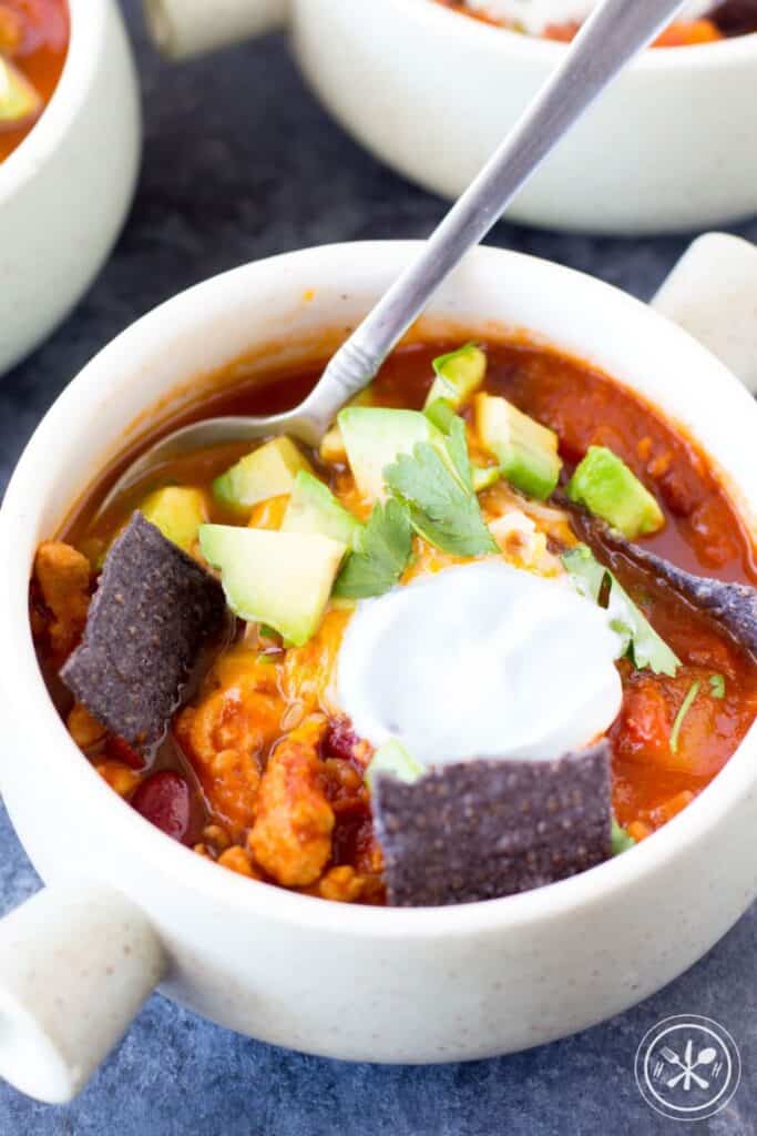 Close up on a bowl of butternut squash turkey chili topped with sour cream and slices of avocado.