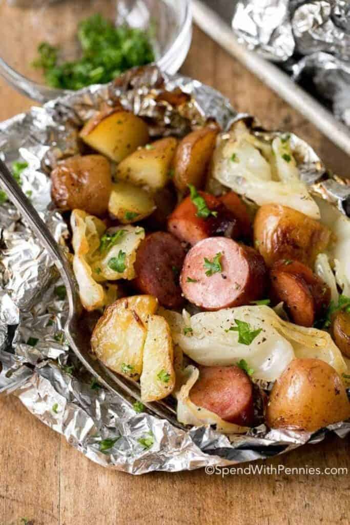 Cabbage and sausage foil packets opened to reveal browned sausage slices, tender cabbage, and roasted baby potatoes seasoned and sprinkled with fresh parsley. An easy family camping meal cooked in foil for simple prep, flavorful results, and quick cleanup at the campsite.