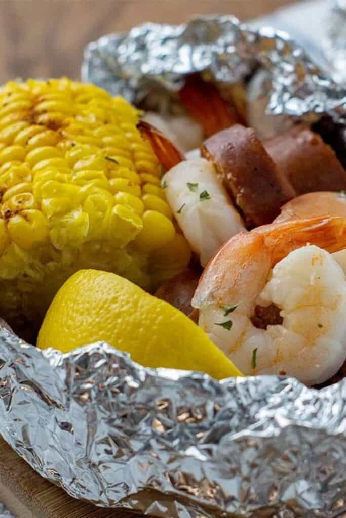 Tin foil wrapped around pieces of corn on the cob and sausage with cajun shrimp. 