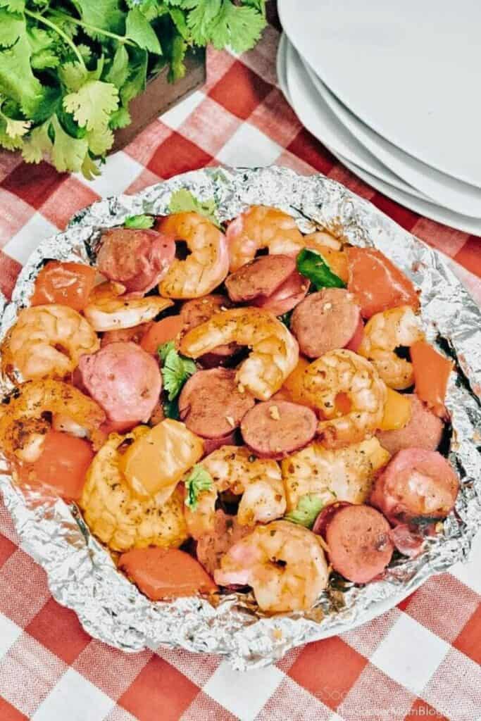 Ocerhead view of a round foil packet full of cajun shrimp boil with corn on the cob pieces, shrimp, sausage rounds and red peppers. 