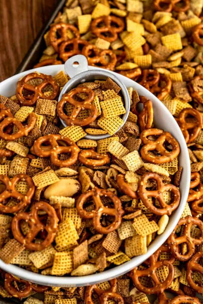 large bowl filled with cajun snack mix made with pretzels, cereal squares, nuts, coated in a savory seasoned blend. The mix is spread across the background emphasizing the variety of textures and bold spiced flavor.