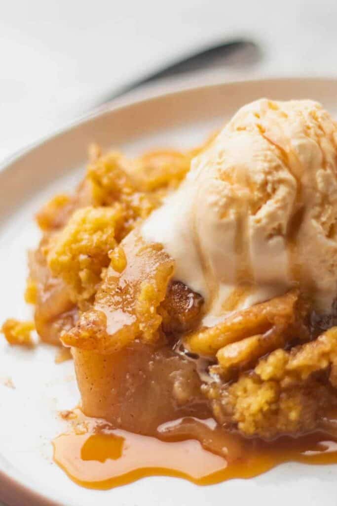 A warm serving of cake mix apple cobbler is topped with a scoop of melting vanilla ice cream, with cinnamon-spiced apples and golden, crumbly cake peeking through