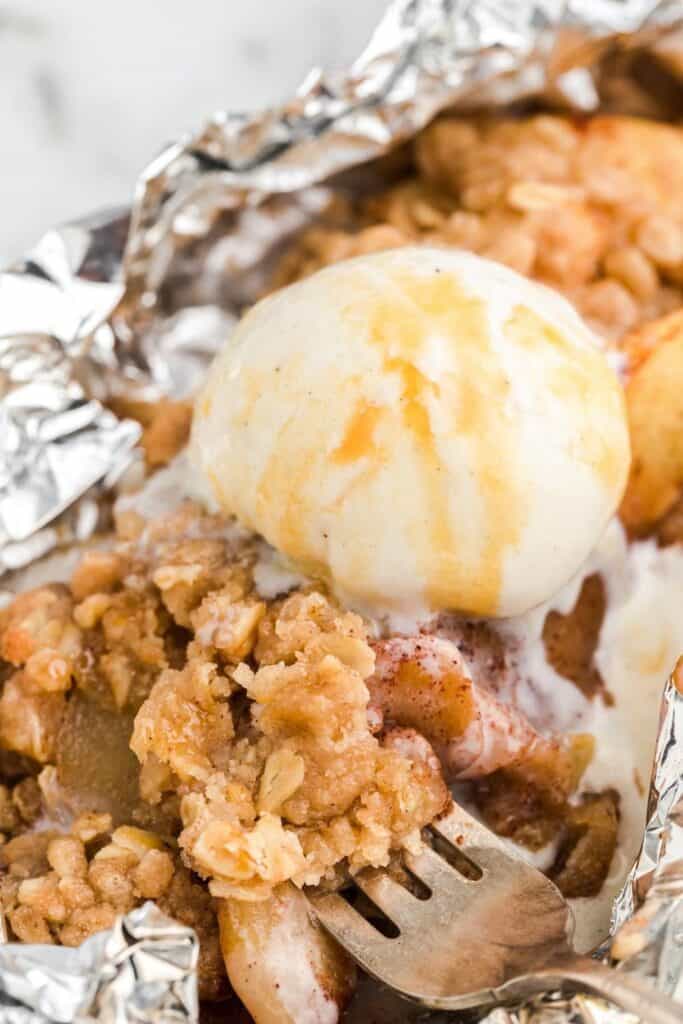 A close up of apple crisp in a foil packet topped with melting ice cream. 
