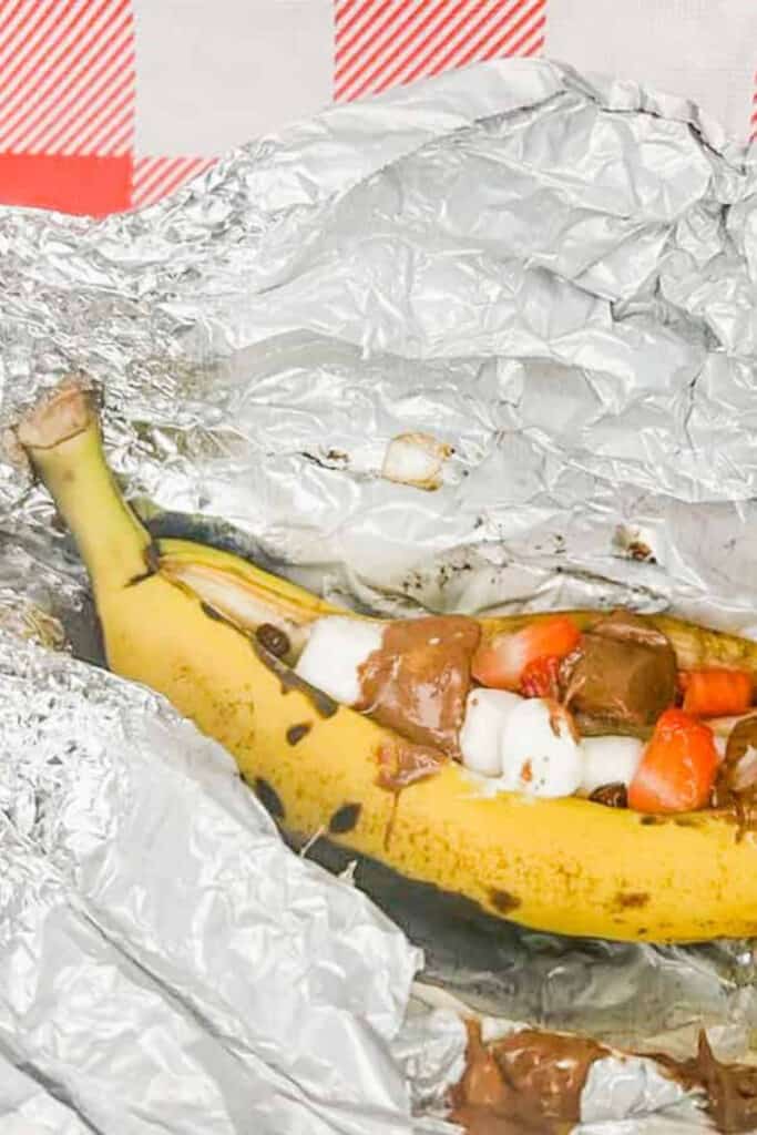 Banana split open and filled with chocolate pieces, mini marshmallows, and sliced strawberries, wrapped in foil for cooking over a campfire. This easy campfire banana boat dessert is a fun and kid-friendly treat perfect for camping trips.