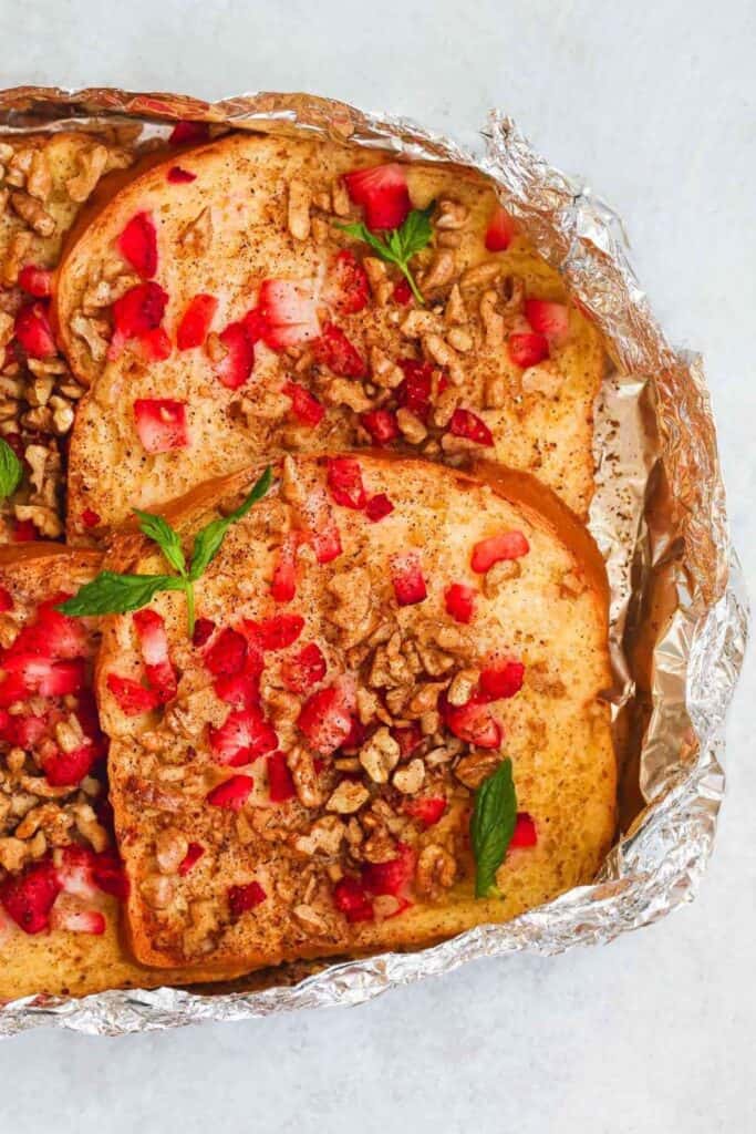 4 pieces of campfire french toast in tin foil packets with diced strawberries, walnuts, and ground cinnamon.