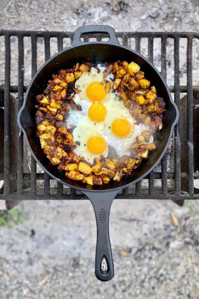 Cast Iron pan over a campfire with potato, sausage, and eggs.