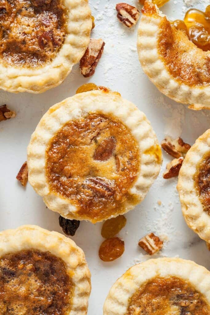 6 Canadian butter tarts with raisins and pecans on a counter top.