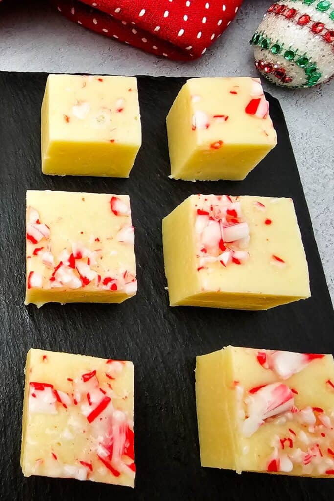 Close-up of six square pieces of candy cane peppermint fudge on a black slate tray, each topped with crushed red and white peppermint candy.