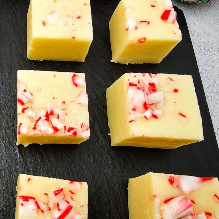 Close-up of six square pieces of candy cane peppermint fudge on a black slate tray, each topped with crushed red and white peppermint candy.
